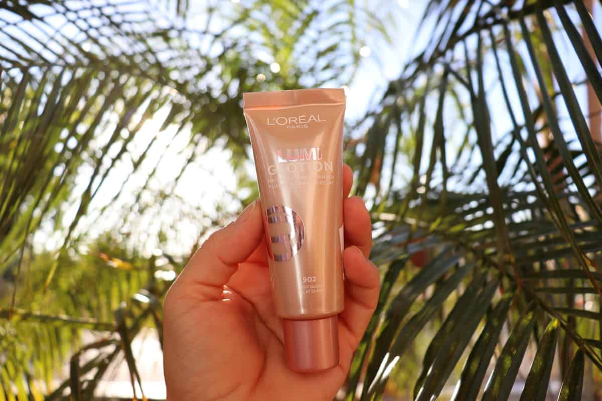L'Oréal Lumi Glotion held by a hand with tropical palm leaves background, bright and vibrant.