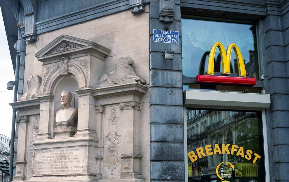 A historic building corner in Brussels featuring a McDonald's sign and a classical sculpture.