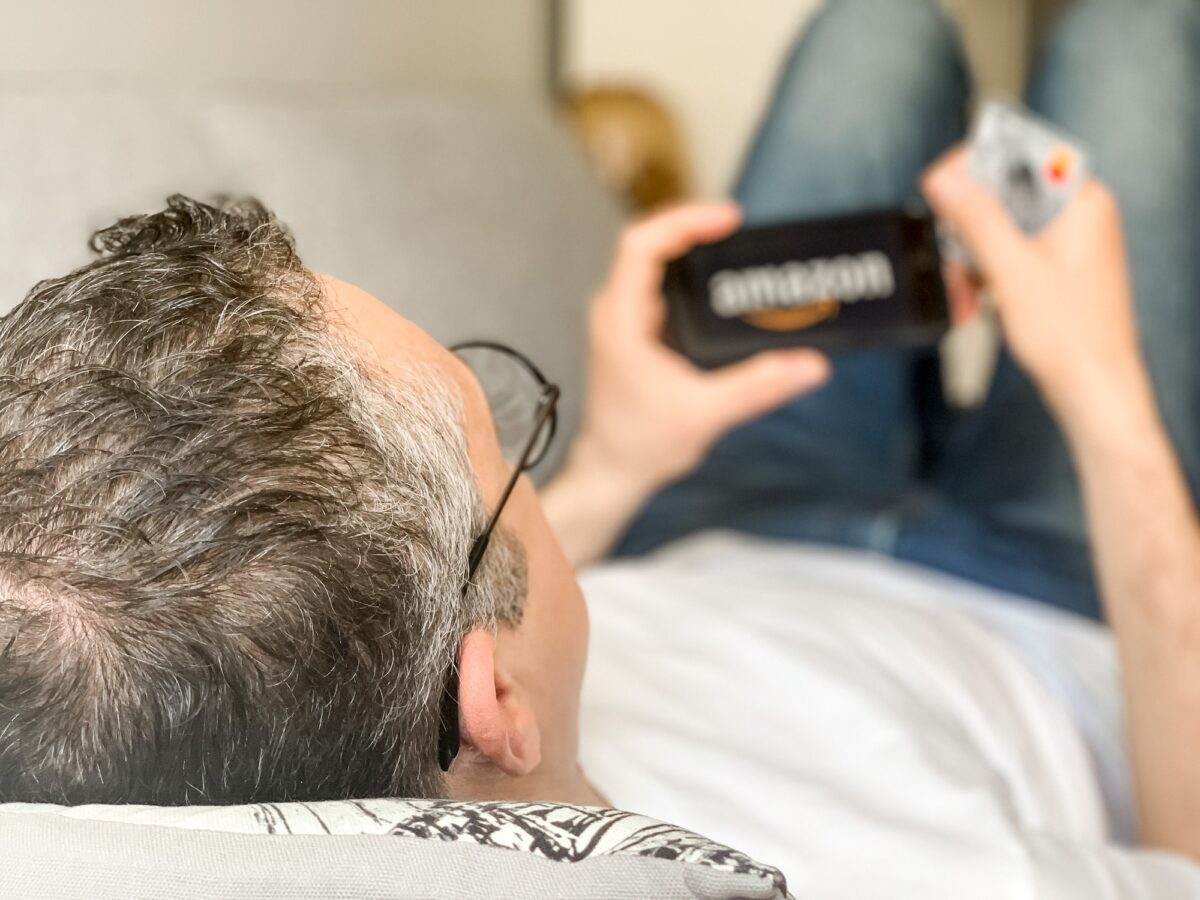 Un homme adulte d'âge moyen fait des achats en ligne sur Amazon en utilisant son téléphone portable pour payer par carte de crédit.